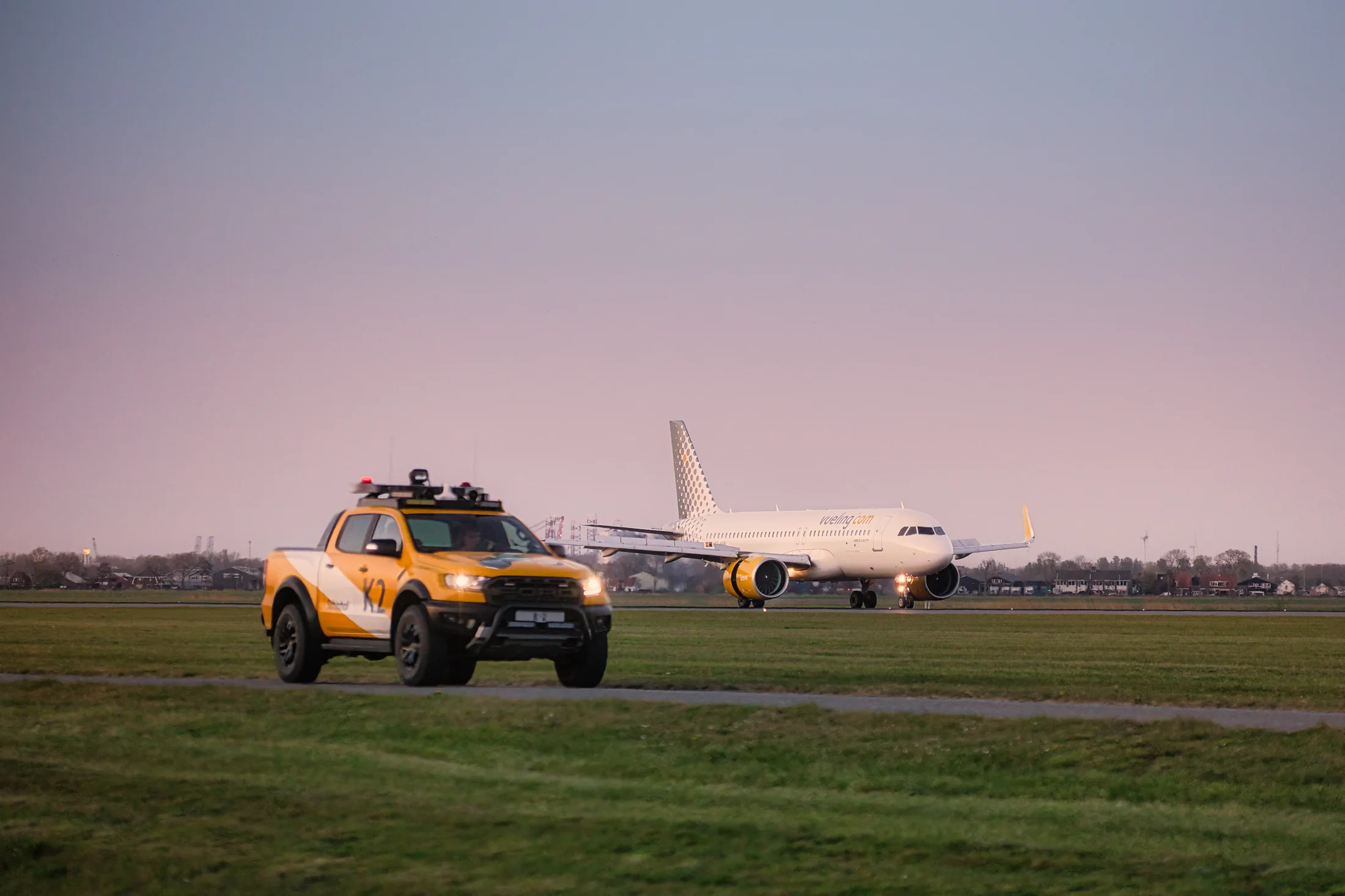 Vueling-Airbus EC-NDB auf dem Vorfeld, begleitet von einem gelben Flughafenfahrzeug.