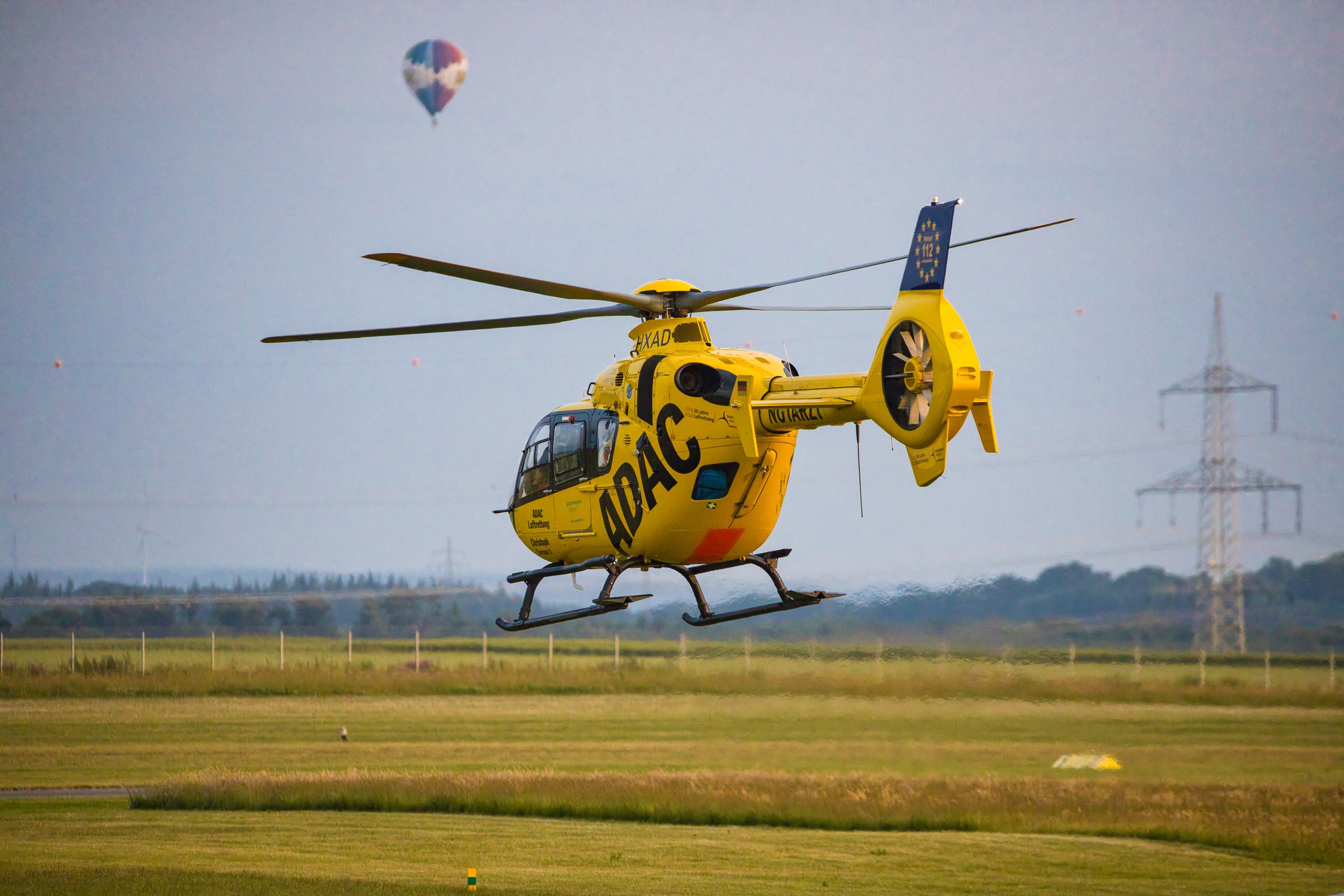 D-HXAD im Flug mit Heißluftballon und Platz im Hintergrund.