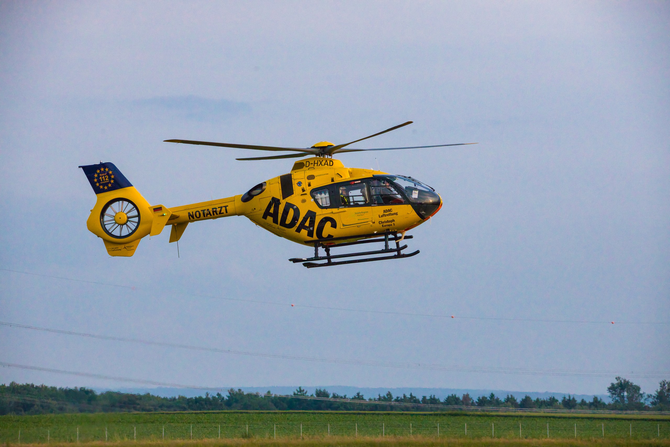 D-HXAD im Flug vor offenem Himmel und Landschaft.