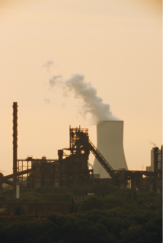 Blick vom Landschaftspark Duisburg-Nord auf Industrieanlagen und einen Kühlturm im warmen Abendlicht