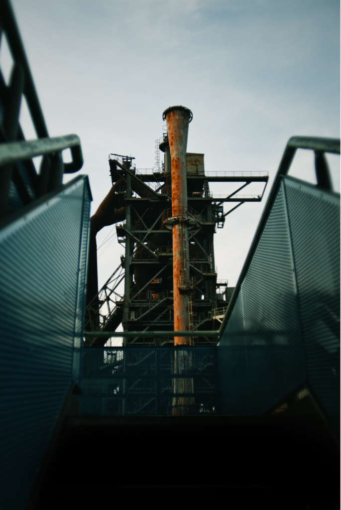 Blick über eine Stahltreppe auf eine alte Industrieanlage mit rostigem Rohr im Landschaftspark Duisburg