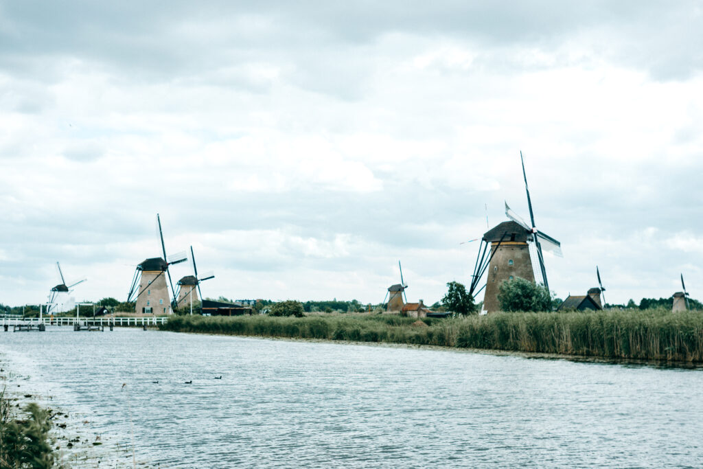 Mehrere historische Windmühlen in Kinderdijk entlang eines breiten Wasserlaufs unter bewölktem Himmel
