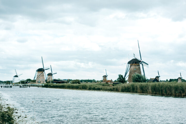 Mehrere historische Windmühlen in Kinderdijk entlang eines breiten Wasserlaufs unter bewölktem Himmel