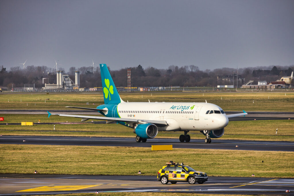 Aer Lingus Airbus A320-214 EI-DEP rollt am Düsseldorfer Flughafen an einem Vorfeldfahrzeug vorbei.